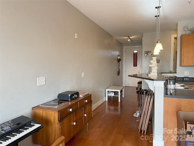 kitchen with wood finished floors, baseboards, brown cabinets, dark countertops, and decorative light fixtures