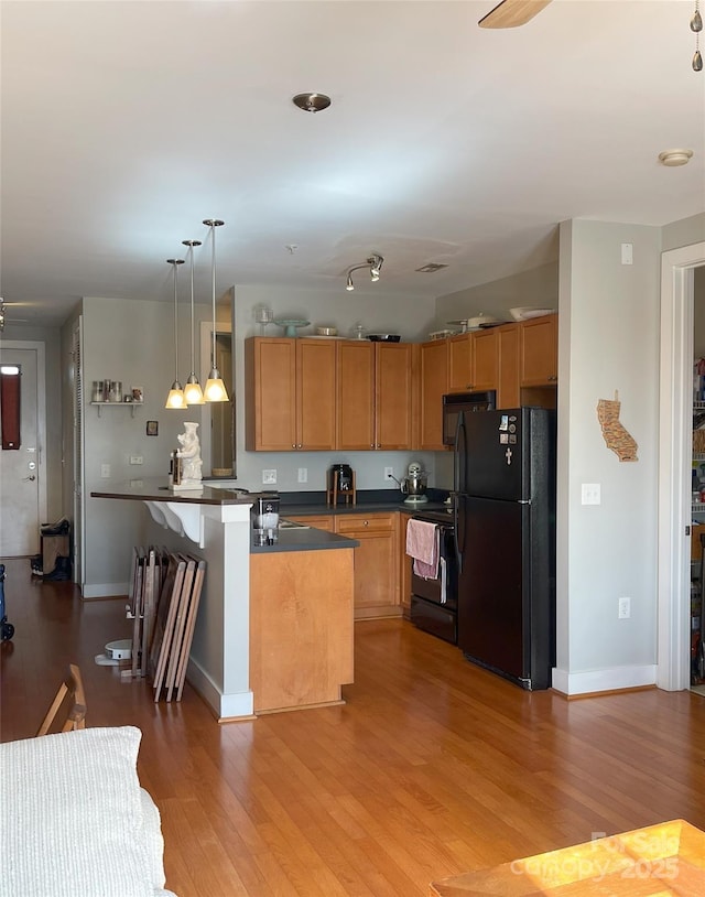 kitchen with dark countertops, black appliances, wood finished floors, and hanging light fixtures