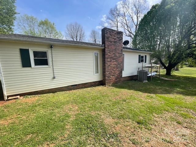 exterior space featuring crawl space, a yard, a chimney, and central AC unit