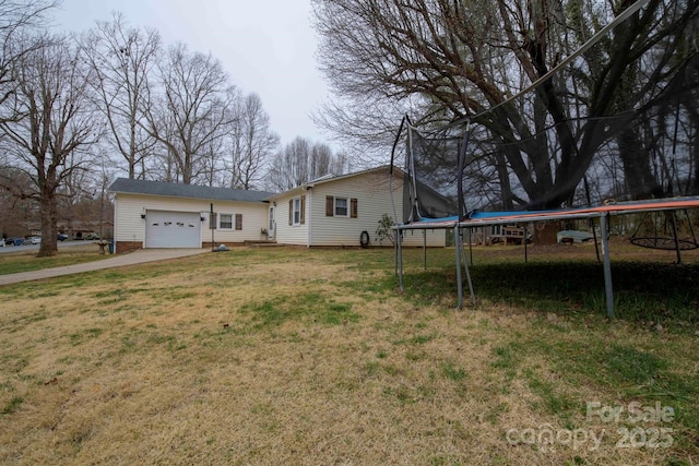 view of front of home with a trampoline, an attached garage, driveway, and a front lawn