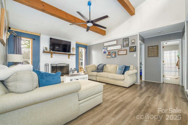 living area featuring vaulted ceiling with beams, a brick fireplace, a ceiling fan, and wood finished floors