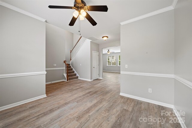 spare room with ceiling fan, stairs, wood finished floors, baseboards, and crown molding