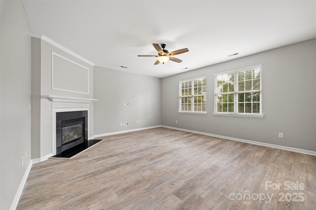 unfurnished living room with ceiling fan, light wood-style flooring, baseboards, a glass covered fireplace, and ornamental molding