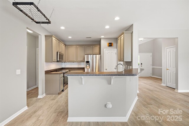 kitchen with appliances with stainless steel finishes, a peninsula, light wood finished floors, a breakfast bar, and baseboards
