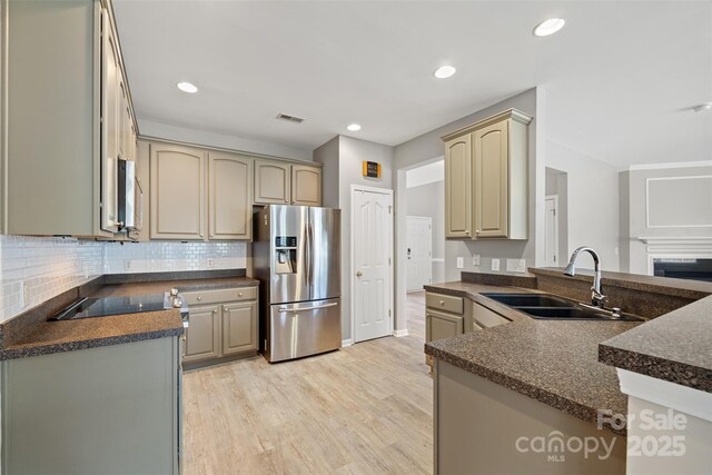 kitchen featuring stainless steel appliances, a sink, light wood-type flooring, a peninsula, and backsplash