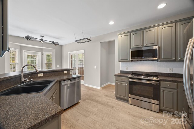 kitchen featuring stainless steel appliances, a sink, decorative backsplash, dark countertops, and recessed lighting