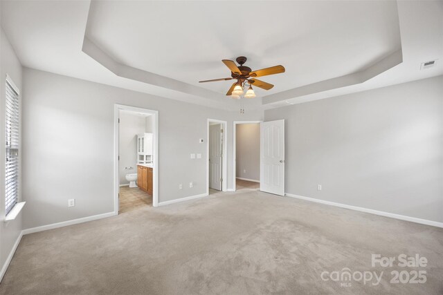 unfurnished bedroom featuring a tray ceiling, multiple windows, and baseboards