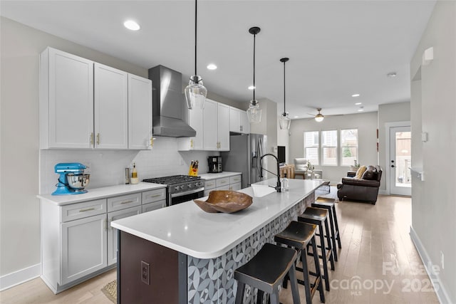 kitchen featuring a kitchen island with sink, a kitchen breakfast bar, tasteful backsplash, appliances with stainless steel finishes, and wall chimney range hood