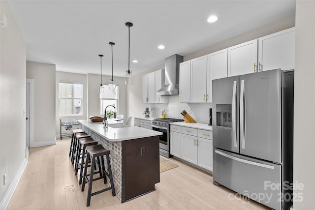 kitchen featuring a center island with sink, stainless steel appliances, decorative backsplash, wall chimney exhaust hood, and light wood-type flooring