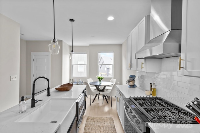 kitchen with stainless steel gas stove, white cabinetry, wall chimney exhaust hood, and a sink