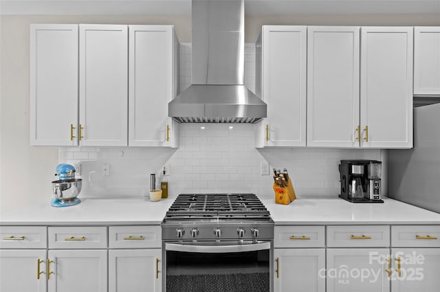 kitchen with white cabinetry, light countertops, wall chimney range hood, and stainless steel gas range