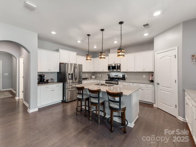 kitchen featuring arched walkways, visible vents, a kitchen breakfast bar, appliances with stainless steel finishes, and dark wood-style floors