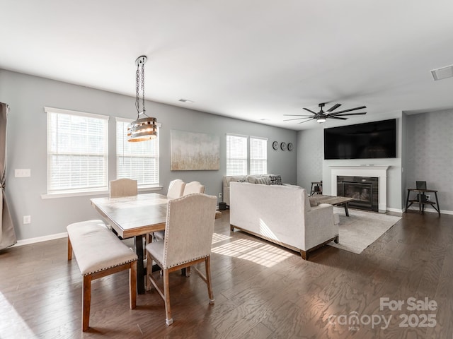 dining area featuring visible vents, baseboards, a ceiling fan, a glass covered fireplace, and dark wood-style floors