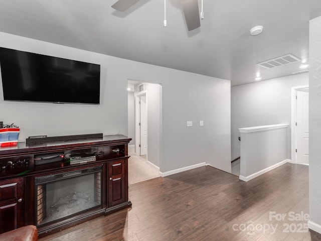 living area featuring baseboards, visible vents, ceiling fan, and dark wood-style flooring