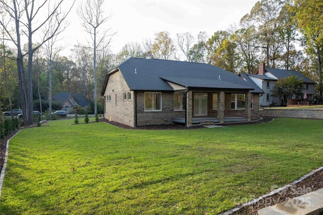 view of front of house with covered porch, brick siding, a front lawn, and roof with shingles