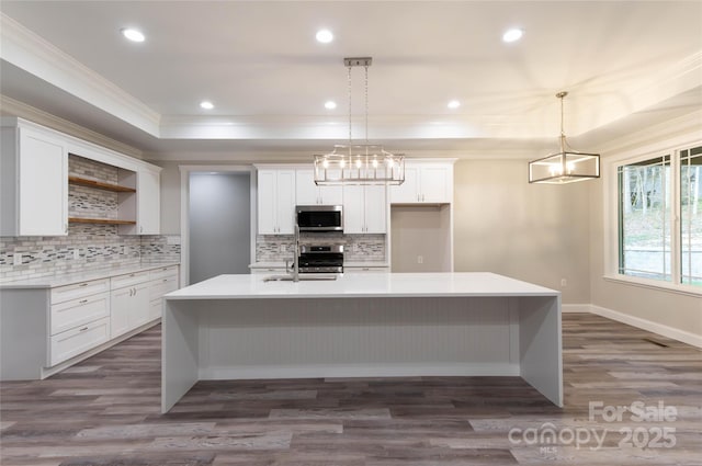 kitchen featuring appliances with stainless steel finishes, ornamental molding, a tray ceiling, a large island with sink, and open shelves