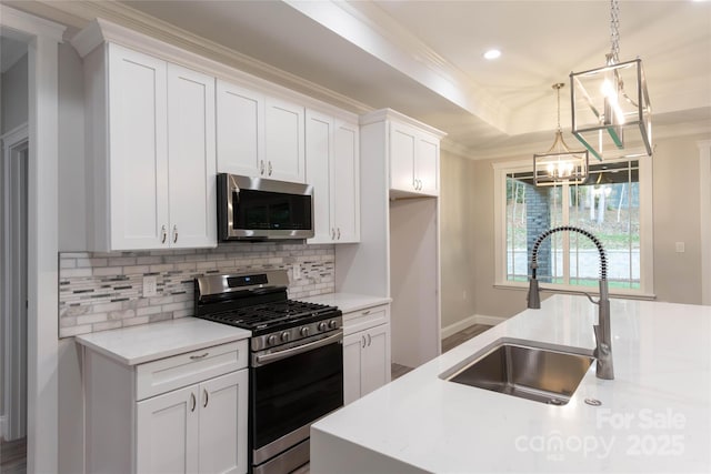 kitchen with a raised ceiling, ornamental molding, light countertops, stainless steel appliances, and a sink