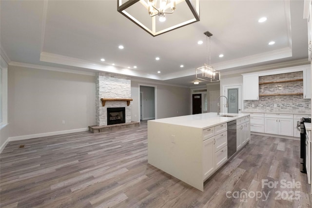 kitchen with a stone fireplace, a tray ceiling, a sink, and a center island with sink