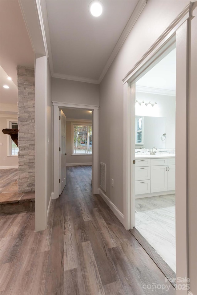 hallway featuring baseboards, light wood-style floors, visible vents, and crown molding