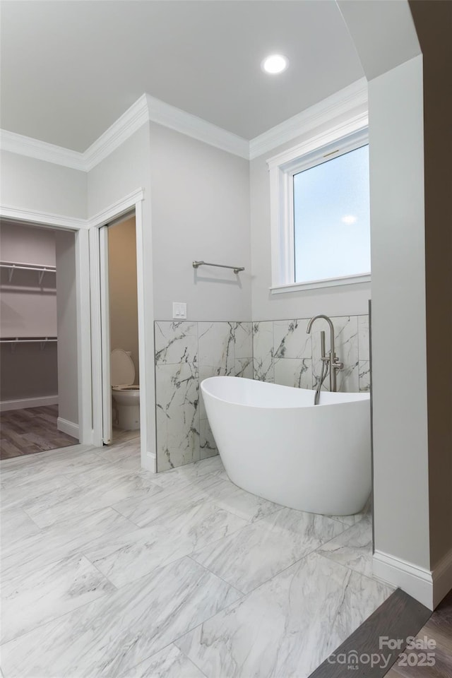 bathroom with a soaking tub, ornamental molding, marble finish floor, and a wainscoted wall