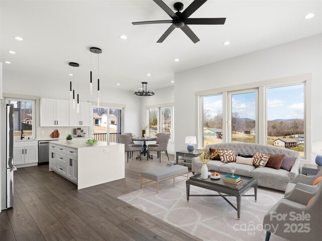 living area with ceiling fan with notable chandelier, dark wood-type flooring, and recessed lighting