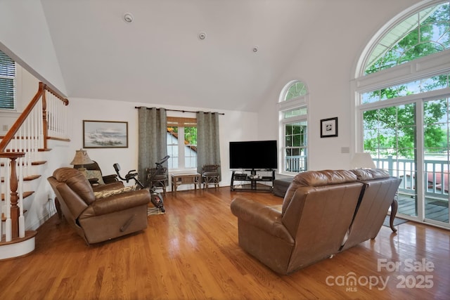 living area featuring high vaulted ceiling, stairs, and wood finished floors