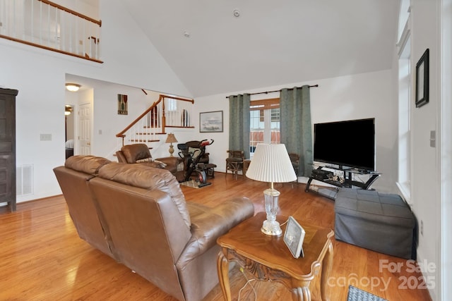 living room with light wood finished floors, stairway, visible vents, and high vaulted ceiling