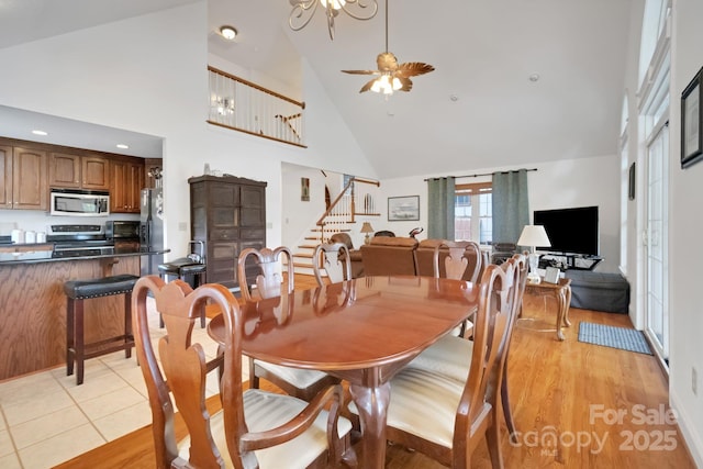 dining space featuring stairs, ceiling fan, high vaulted ceiling, and light wood-style flooring