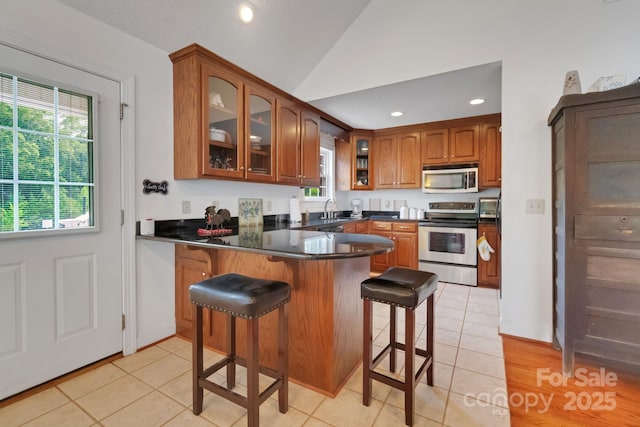 kitchen with lofted ceiling, glass insert cabinets, brown cabinets, a peninsula, and stainless steel appliances