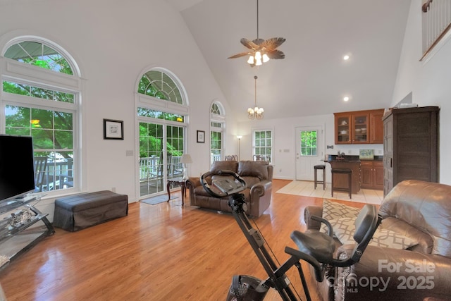 living area with light wood-type flooring, high vaulted ceiling, and ceiling fan with notable chandelier