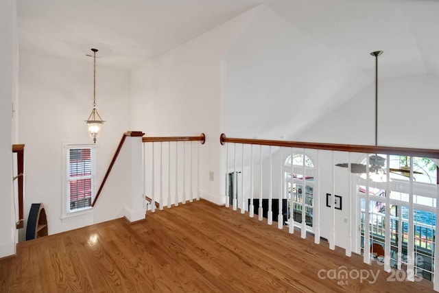 hallway with a healthy amount of sunlight, vaulted ceiling, an upstairs landing, and wood finished floors