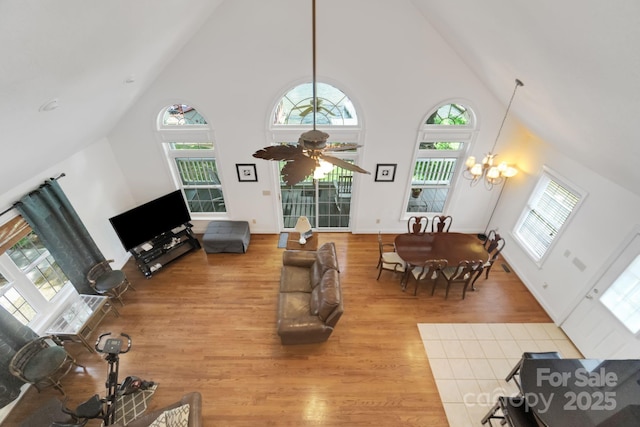 living room featuring ceiling fan with notable chandelier, high vaulted ceiling, light wood-style flooring, and baseboards