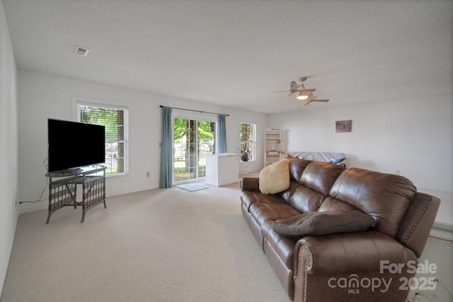 living area with visible vents, ceiling fan, and light carpet