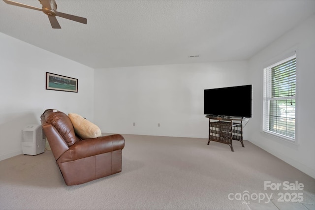 living room featuring carpet floors, visible vents, a ceiling fan, and a textured ceiling