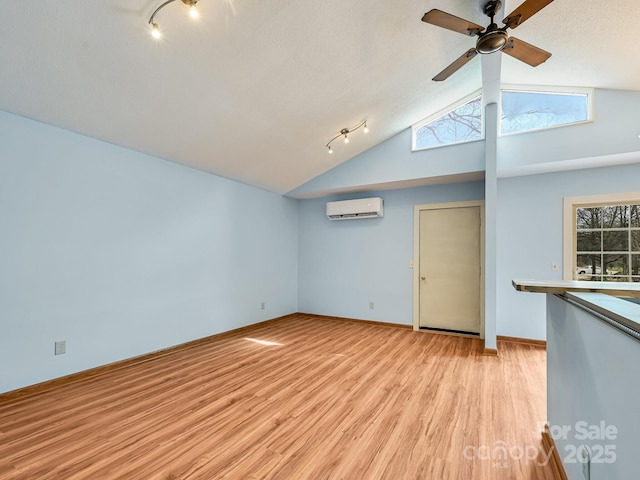 unfurnished room with baseboards, ceiling fan, an AC wall unit, light wood-type flooring, and lofted ceiling