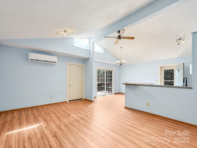 spare room with an AC wall unit, light wood-style flooring, ceiling fan with notable chandelier, and a textured ceiling