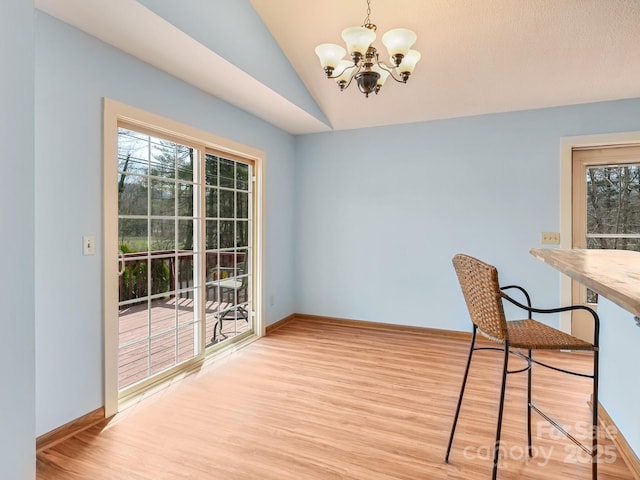 unfurnished dining area featuring baseboards, light wood-type flooring, lofted ceiling, and an inviting chandelier