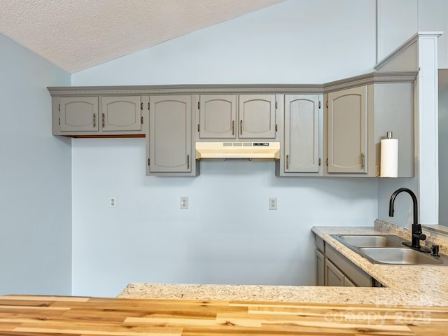 kitchen featuring gray cabinets, a sink, vaulted ceiling, light countertops, and under cabinet range hood