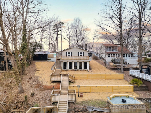 back of house at dusk featuring a jacuzzi, an outdoor structure, fence, stairs, and a wooden deck