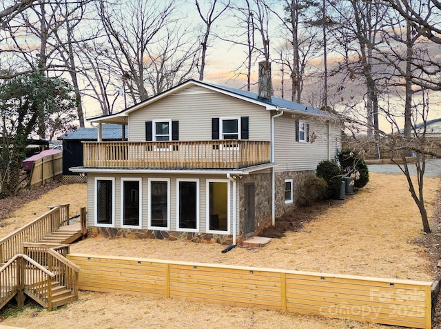 back of property at dusk with stairway, a chimney, fence, and a wooden deck