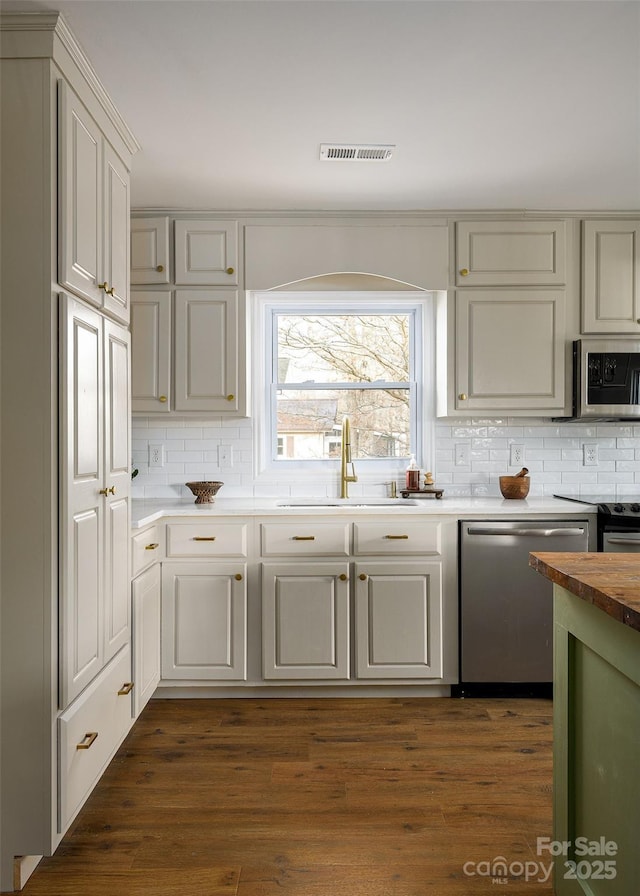 kitchen featuring stainless steel appliances, dark wood-type flooring, a sink, visible vents, and tasteful backsplash