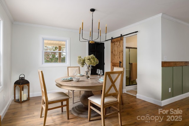 dining area with a barn door, ornamental molding, and wood finished floors