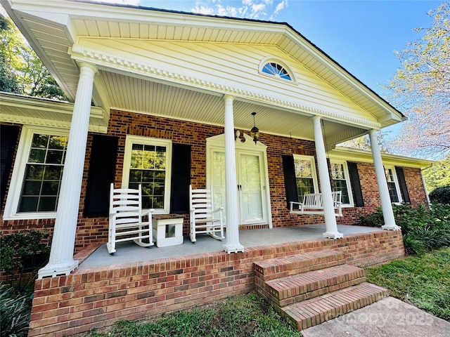 doorway to property featuring covered porch and brick siding