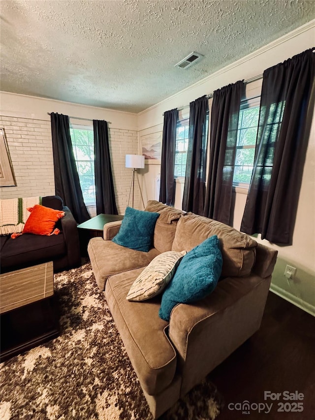 living room with a healthy amount of sunlight, brick wall, visible vents, and a textured ceiling