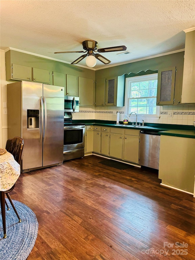 kitchen with a sink, crown molding, appliances with stainless steel finishes, and dark wood-type flooring