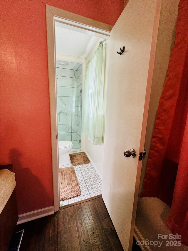 full bathroom with a stall shower, wood finished floors, toilet, and baseboards