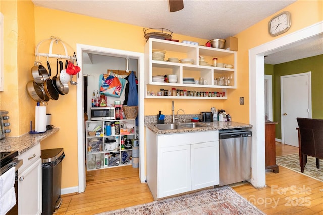 kitchen with light wood finished floors, appliances with stainless steel finishes, a sink, and white cabinetry