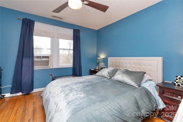 bedroom featuring visible vents, hardwood / wood-style flooring, ceiling fan, a textured ceiling, and cooling unit