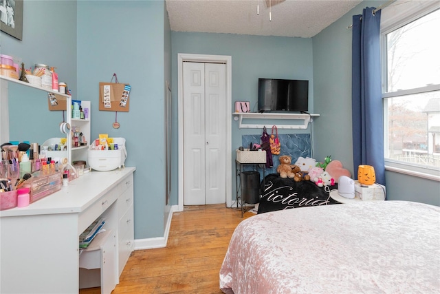 bedroom featuring a textured ceiling, multiple windows, a closet, and light wood-style flooring