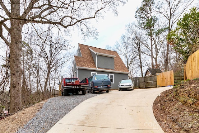 view of side of property with concrete driveway, roof with shingles, fence, and stucco siding